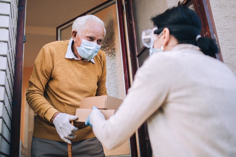 A person delivering a meal to an elderly man.