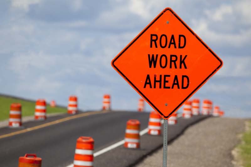 A highway with road cones and a sign that reads Road Work Ahead. 