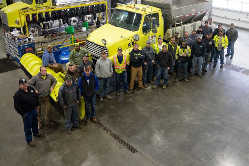 St. Croix County Snowplow Drivers standing next to a snowplow in a garage. 