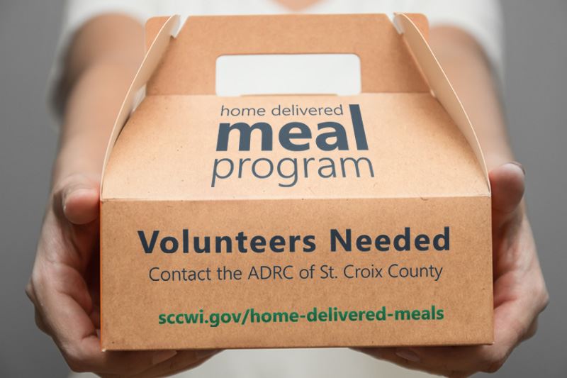 A person holding a box for home delivered meals with the text volunteers needed.