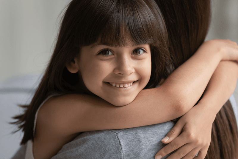 A child smiling and hugging an adult.